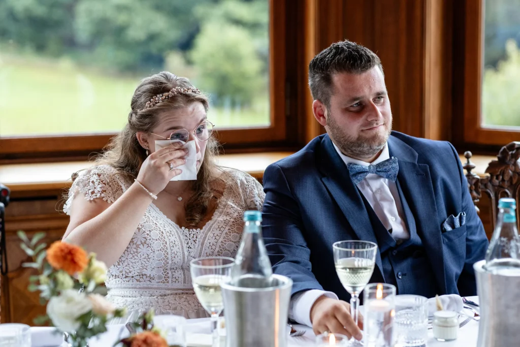 Hochzeitsfotograf Trier Luxemburg - Brautpaar sitzt am Tisch und während einer emotionalen Rede muss die Braut sich die Tränen wegwischen.