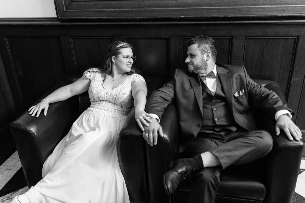 Hochzeitsfotograf Trier Luxemburg - Das Brautpaar sitzt beim Foto-Shooting entspannt auf ledernen Sesseln in der Location und guckt sich innig in die Augen. Schwarz-weiss Foto.