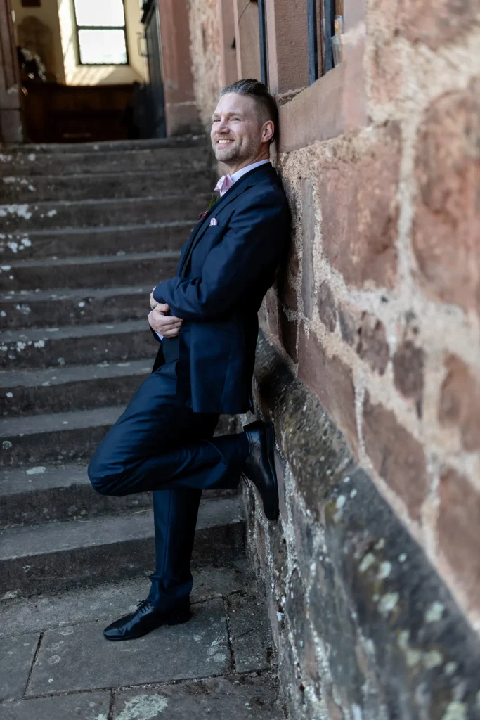 Hochzeitsfotograf Trier Luxemburg - Portrait vom Bräutigam, wie er lässig an der Wand von Schloss Hamm lehnt