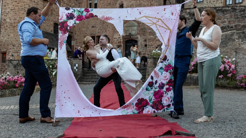 Hochzeitsfotograf Trier Luxemburg - Der Bräutigam trägt seine Braut durch das ausgeschnittene Herz des Bettlakens.