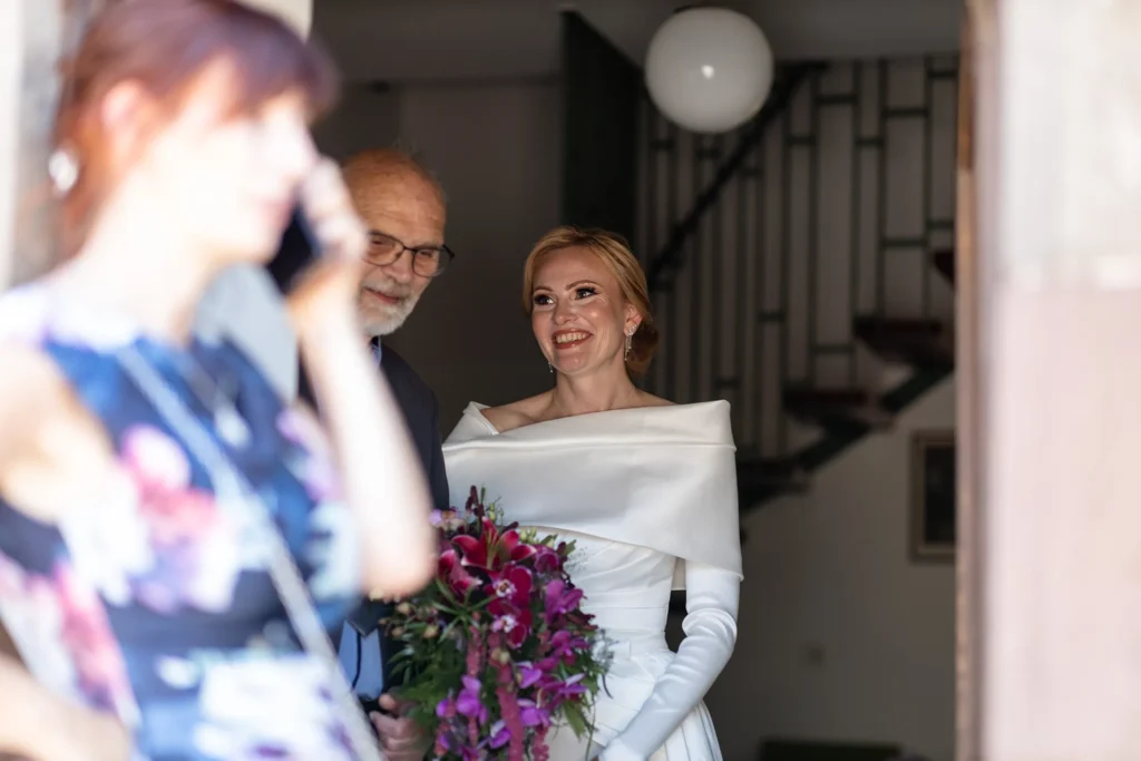 Hochzeitsfotograf Trier Luxemburg - Trauzeugin telefoniert draussen, während drinnen die gut gelaunte Braut mit ihrem Vater zu sehen ist.